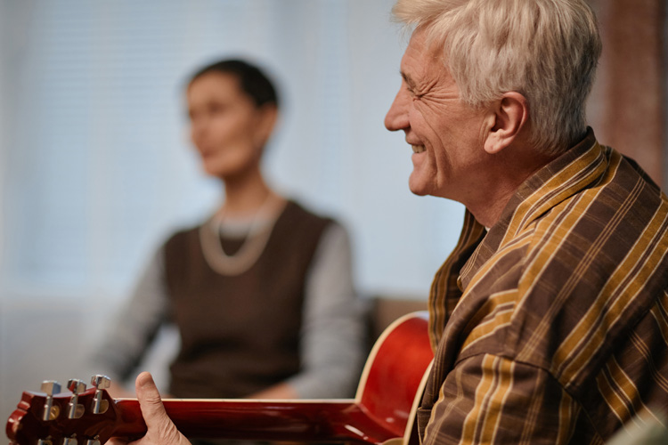 Cappella Pueblo West Senior Living Community in Pueblo West, CO - cappella of pueblo west senior man playing guitar and smiling Cappella Pueblo West Senior Living Community in Pueblo West, CO - cappella of pueblo west senior man playing guitar and smiling